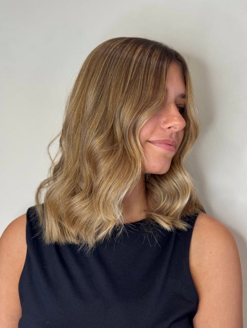 Woman with shoulder-length blonde wavy hair wearing a black sleeveless top