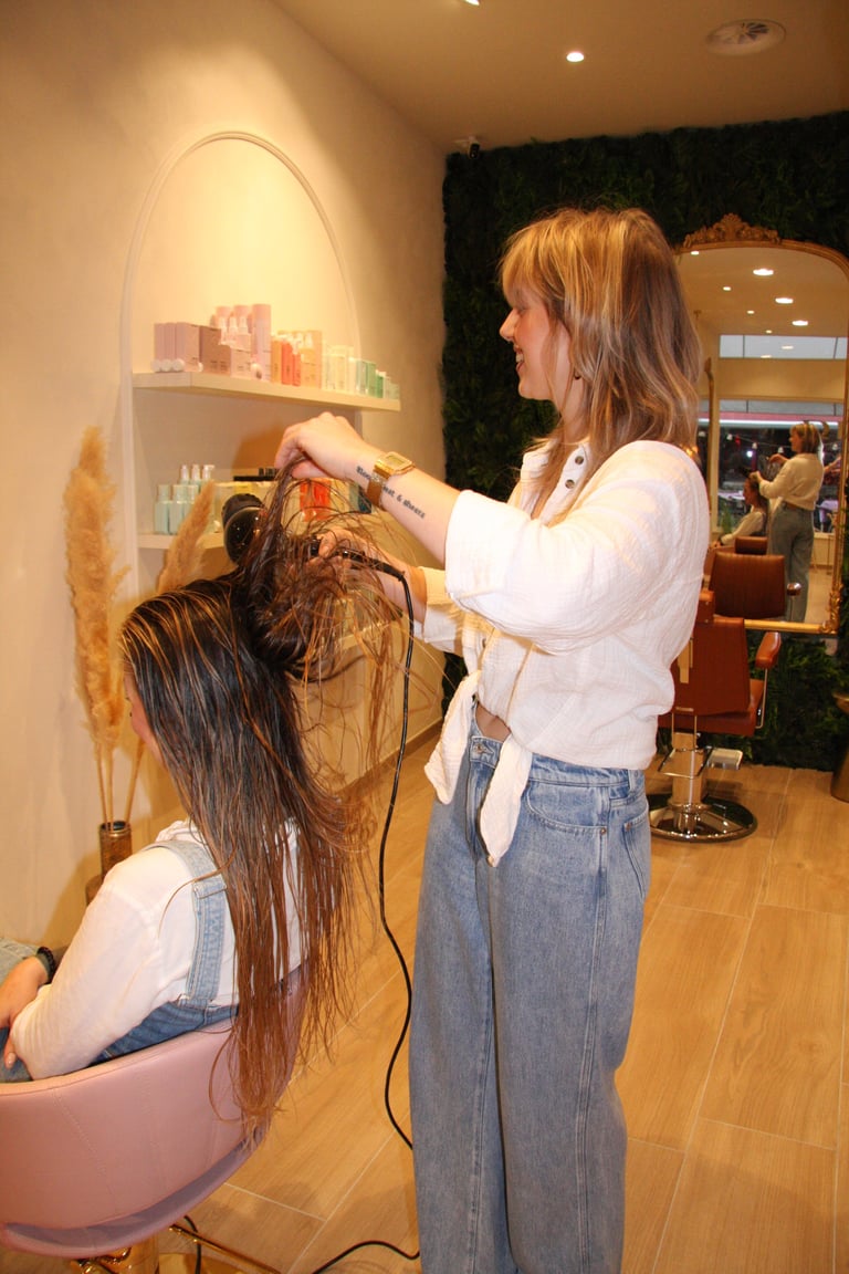Hairstylist applying hair treatment to client with wet brown hair in a modern salon setting
