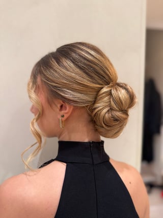 Woman with blonde hair styled in an updo bun, wearing a black sleeveless top, shown from behind